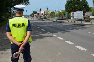 Policjant stoi na drodze, w ręce trzyma tarczę do zatrzymywania pojazdów.