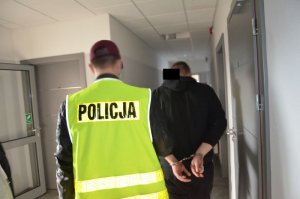 Policjant prowadzi zatrzymanego korytarzem