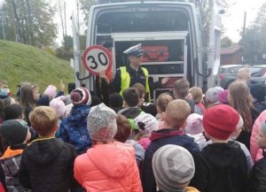 Policjant ruchu drogowego prezentuje radiowóz - Policyjny Ambulans Ruchu Drogowego. Wokół samochodu przy policjanci stoją dzieci.