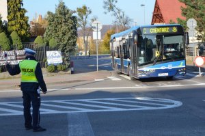 Policjant zatrzymuje pojazdy jadące za nim, ponieważ umożliwia przejazd autobusowi, który jedzie z drogi po lewej stronie policjanta przez skrzyżowanie.