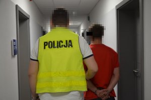 Policjant prowadzi zatrzymanego za przedramię