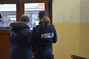 Policjantka rozmawia z kobietą na terenie dworca PKP. Za nimi widoczne są drzwi wejściowe do dworca.