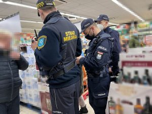 Policjanci ze strażnikiem miejskim kontrolują klienta bez maseczki.