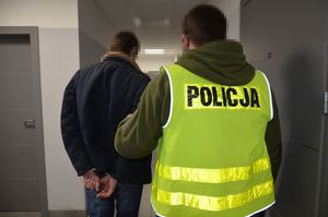 Policjant prowadzi zatrzymanego mężczyznę.