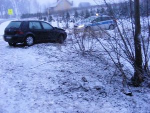 Na poboczu drogi, na śniegu przy zaroślach stoi czarny vw golf a w tle za nim radiowóz.