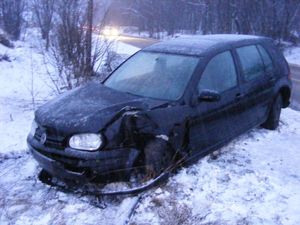 Na poboczu drogi, na śniegu przy zaroślach stoi czarny vw golf.