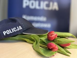 Na biurku leżą tulipany czerwone na nich czapka policyjna z napisem POLICJA , tło jest grantowe