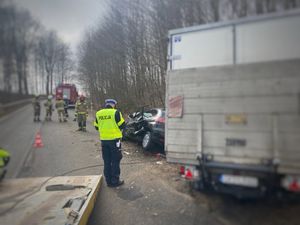 Policjant stoi na jezdni obok rozbitych samochodów.