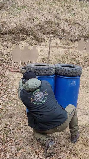 Policjant chowa się za przeszkodą (dwoma beczkami) i z zza nich oddaje strzał w kierunku tarczy.