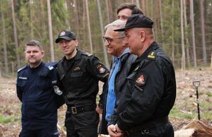 Obok siebie w lesie stoi kilka osób m.n. przedstawiciele służb mundurowych oraz Komendant Powiatowy.