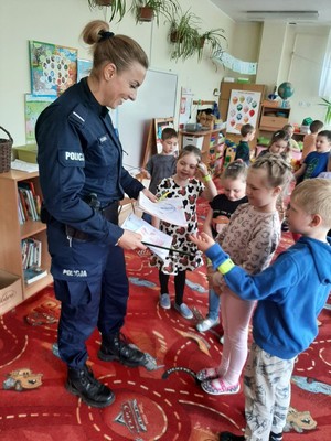 Grupa dzieci wręcza policjantce rysunki.