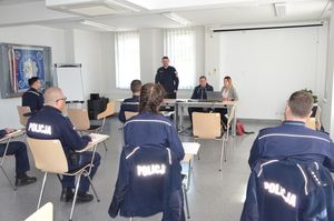 Sala odpraw, komendant przemawia do zebranych na niej osób, obok niego przy długim biurku siedzą przedstawiciele SOK i SKM.