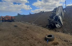 Na pierwszym planie leżąca na skarpie ciężarówka po prawej stronie, w pewnym oddaleniu od niej stoi pod skarpą druga ciężarówka z rozbitym tyłem.