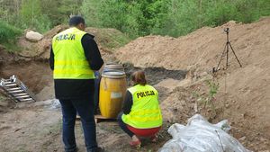 Policjanci wykonują oględziny w miejscu wykopu w ziemi, policjantka kuca a policjant stoi i czemuś się przygląda.