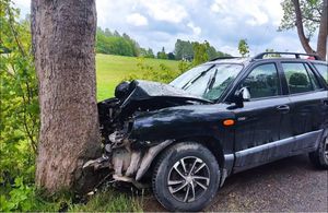 Czarny hyundai stoi przy drzewie, maska pojazdu jest zniszczona - pognieciona po uderzeniu w drzewo.