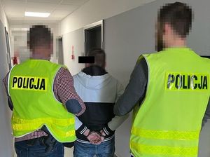 Policjanci prowadzą zatrzymanego mężczyznę korytarzem komendy.