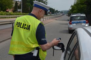 Policjant stoi przy zatrzymanym samochodzie z urządzeniem do badania trzeźwości, kierowca ma otwarte okno