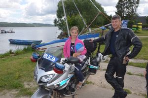 Na motocyklu siedzi uśmiechnięta dziewczynka, pozująca do zdjęcia a obok niej stoi policjant ruchu drogowego.