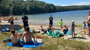 Policjanci chodzą po plaży i rozmawiają z wypoczywającymi osobami, rozdają im ulotki