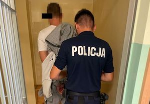 Policjant w celi zakłada kajdanki zatrzymanemu, którego będzie wyprowadzał z obiektu.