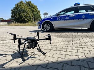 Dron stoi na ziemi a za nim stoi radiowóz