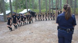 Policjantka stoi po lewej stronie, przed nią i po lewej stronie stoją harcerze.