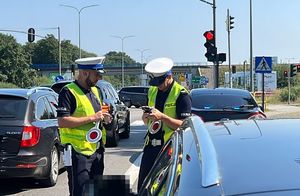 Policjanci stoją przy drodze, kontrolują dokumenty, samochód kontrolowany stoi obok.