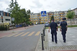 Policjanci idą po chodniku, za nimi widać przejście dla pieszych oraz oznakowanie przejścia