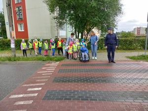 Policjant wraz z grupą dzieci stoi przed przejściem dla pieszych.