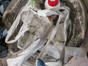 Na zdjęciu widoczne jest wiadro z obsypaną białym proszkiem , w środku znajdują się inne mniejsze foliowe opakowania oraz butelka plastikowa w białym kolorze z nakrętką w kolorze czerwonym. W otwartych foliowych workach widać biały proszek - amfetaminę.