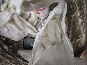 Na zdjęciu widoczne jest wiadro z obsypaną białym proszkiem , w środku znajdują się inne mniejsze foliowe opakowania oraz butelka plastikowa w białym kolorze z nakrętką w kolorze czerwonym. W jednym z opakowań widać zbryloną większą ilość amfetaminy.