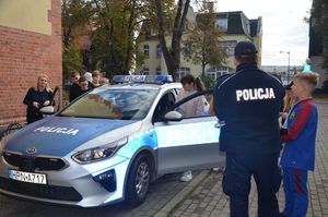 Dzieci oglądają policyjny radiowóz, policjant stoi obok samochodu i rozmawia z kilkorgiem dzieci