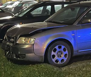 Na zdjęciu widoczny przód rozbitego samochodu audi, który stoi na parkingu.