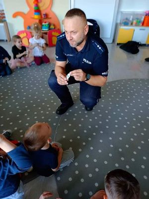 Policjant przykucnął wśród dzieci i z nimi rozmawia