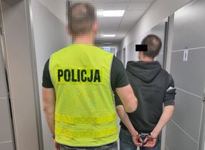 Policjant prowadzą zatrzymanego mężczyznę korytarzem komendy.