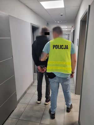 Policjant prowadzą zatrzymanego mężczyznę korytarzem komendy.