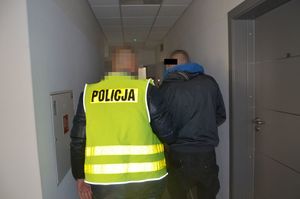 Policjant prowadzi zatrzymanego mężczyznę.