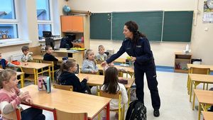 Policjantka podchodzi do ławek dziecięcych i rozdaje odblaski.