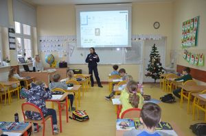 Policjantka prowadzi zajęcia w szkole. Dzieci siedzą w ławkach.