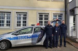 Policjanci stoją przy otwartym radiowozie, do którego włożone zostały paczki