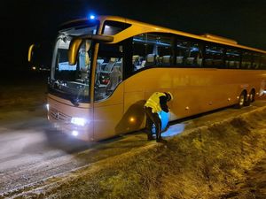 Kontrola autokaru, policjant sprawdza ogumienie w autobusie po lewej stronie pojazdu świeci latarką