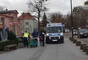 Policjanci rozdają odblaski, obok idących pieszych stoi radiowóz na sygnałach świetlnych