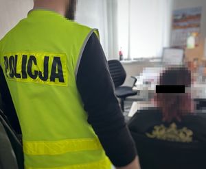 Policjant stoi za kobietą, która jest przesłuchiwana