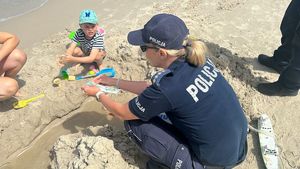 Policjantka rozmawia z turystami na plaży, pokazuje jak korzystać z opaski niezgubki