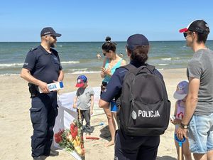 Policjanci rozmawiają z turystami, opowiadają o bezpieczeństwie a dzieciom przekazują opaski niezgubki.