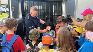 Policjant zakłada jednemu z dzieci czarny kask ochronny.