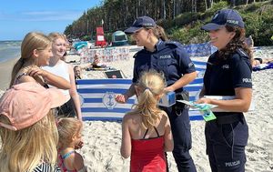 Policjantki rozmawiają z dziećmi, rozdają opaski niezgubki.