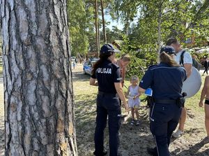 Policjanci przy plaży wręczają dzieciom opaski niezgubki.