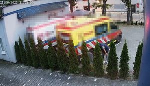 Dwa ambulansy stoją za żywopłotem. Za jedną z roślin widać schylającego się mężczyznę, przy jednej z karetek.