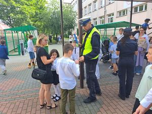 Policjanci przy szkole rozdają dzieciom odblaski.